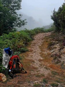 Foggy trail scene with a lone backpack and hiking gear on a misty path.